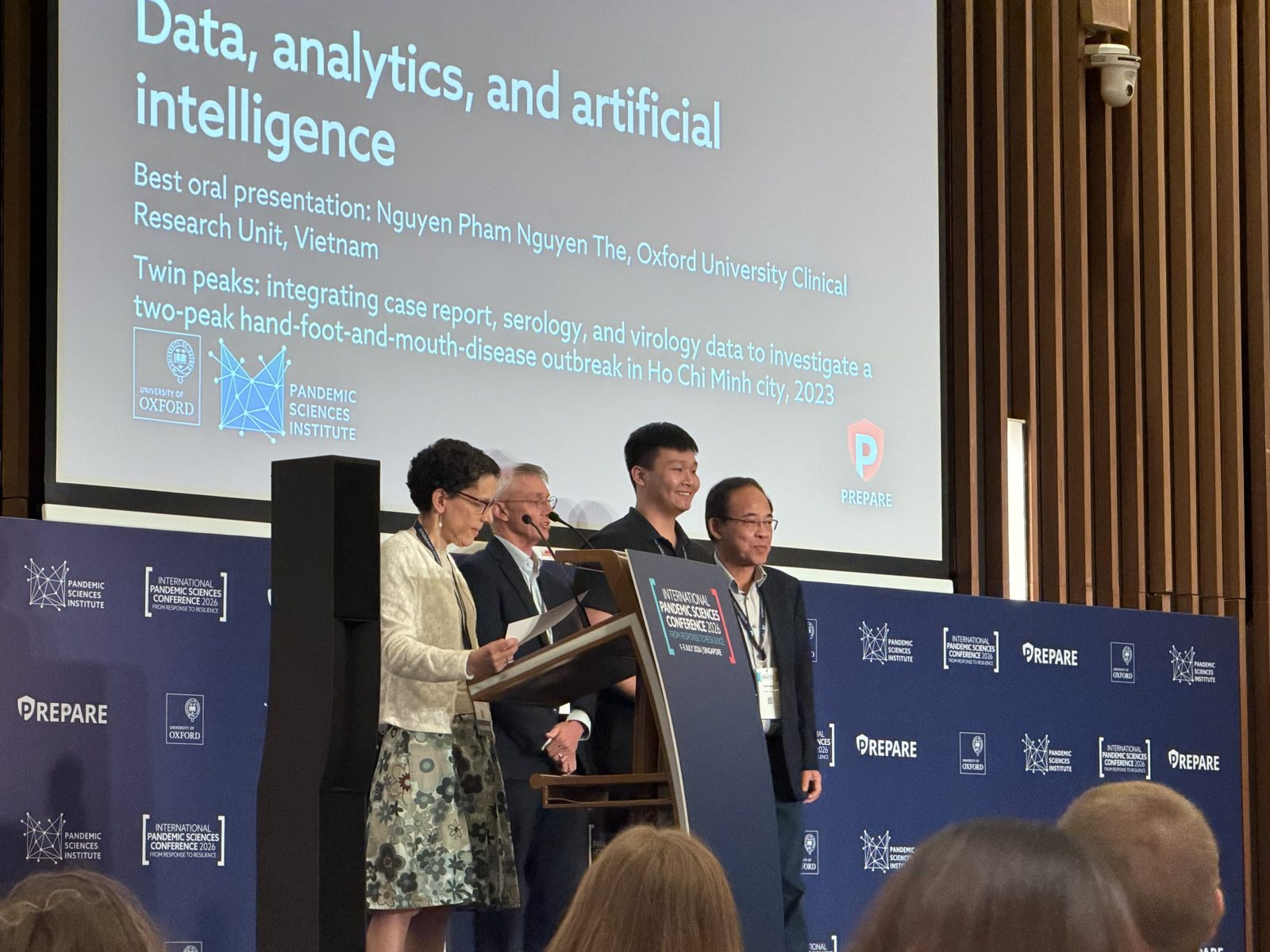 Phạm Nguyễn Thế Nguyên stands on stage with other award recipients at the International Pandemic Sciences Conference 2026, in front of a slide reading Data, analytics, and artificial intelligence.